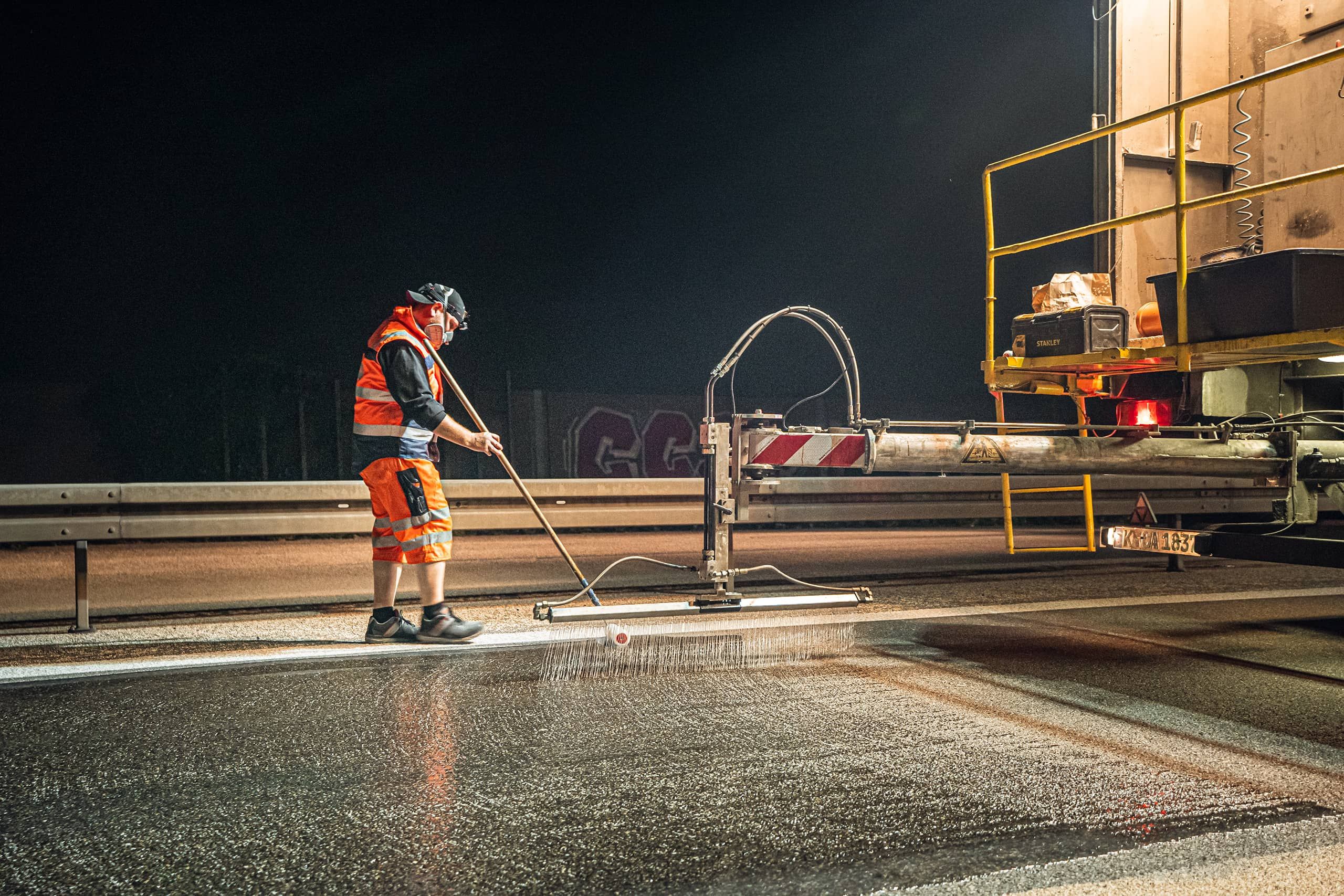 Auftrag des Reaktionsharzes Arbeiter in Schutzkleidung bei Nacht auf Autobahn bei Auftrag des Reaktionsharzes